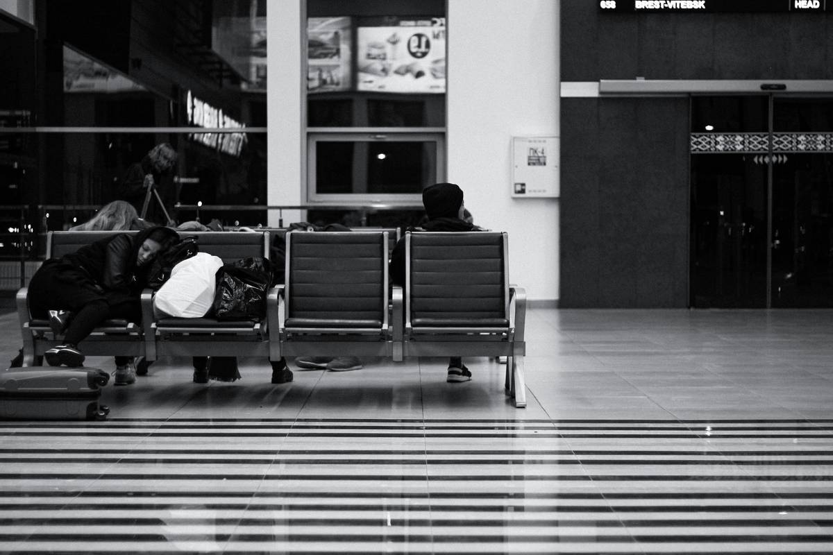Man sitting on luggage looking frustrated at a crowded airport