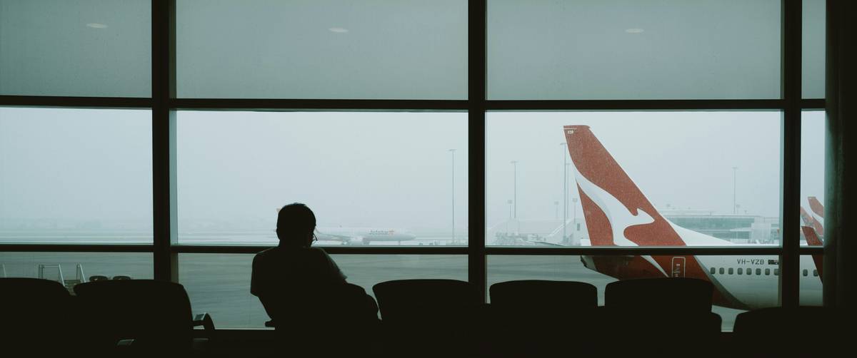 Traveler sitting on luggage near gate sign displaying delayed message